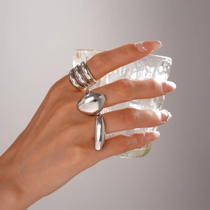 Detailed view of three-piece silver minimalist metal rings worn by model holding glass