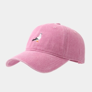 Dettaglio del cappellino rosa in cotone lavato con ricamo di piccione e texture vintage
