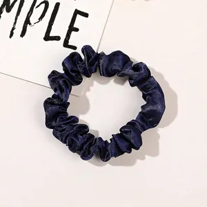 Detail of navy blue satin scrunchie with glossy texture and elastic pleated design
