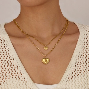 Detail of layered gold stainless steel necklace with textured heart pendants on a model