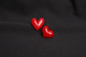 Detail of glossy bright red heart-shaped badges on dark grey knitted fabric background