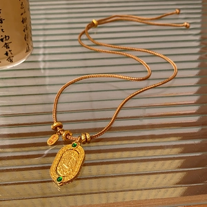 Detailed macro view of an oval gold-plated pendant with green stones and woven rope