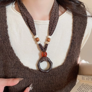Detail of fabric print necklace with wooden beads and amber pendant on knitwear