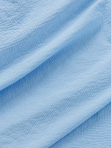 Macro shot of light blue polo shirt fabric featuring a unique textured waffle weave pattern