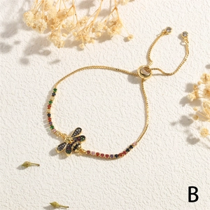 Detail of adjustable gold bee bracelet with colorful cubic zirconia on textured background