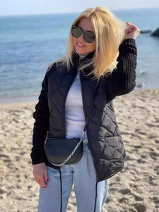 Women's black quilted jacket with knit sleeves and zipper, shown in outdoor beach setting