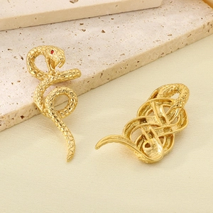 Detailed view of two 18k gold snake-shaped pendants with red eyes on a stone surface