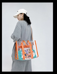 Detailed view of clear PVC tote bag with orange trim worn on a model's shoulder