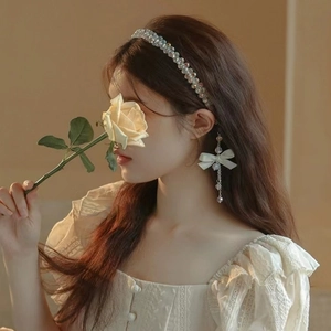 Close-up of beaded headband and white bow ribbon earrings with long tassels on model