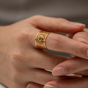 Vintage gold hollow-out ring with green gemstone on model hand in a warm aesthetic view