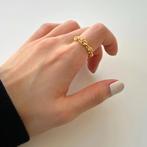 Detailed view of a gold braided chain ring worn by a model in a minimalist setting