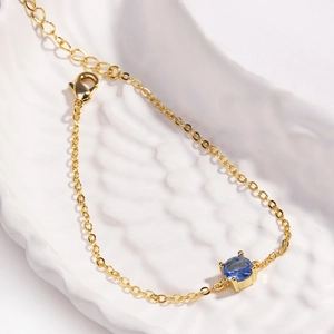Detail of adjustable gold chain bracelet featuring a blue round-cut gemstone and lobster clasp