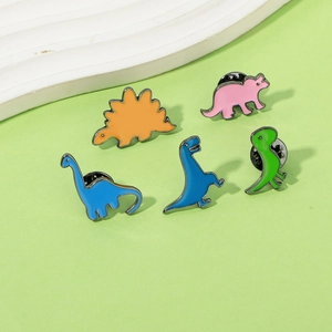 Five colorful enamel dinosaur brooches in orange, pink and blue on green surface
