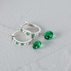 Macro shot of silver hoop earrings featuring emerald green round crystals and small zircons