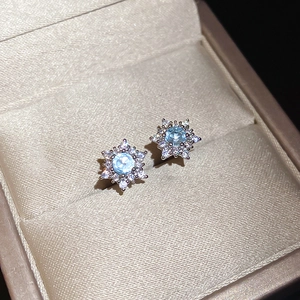 Macro view of snowflake stud earrings with light blue gemstone and shimmering zircon pavé