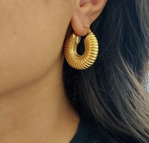 Detail view of gold chunky hoop earrings with spiral texture on female model's ear