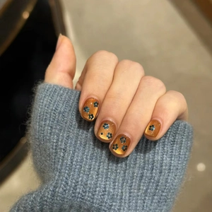 Cat eye nail press-ons with blue floral patterns on amber base shown on hands