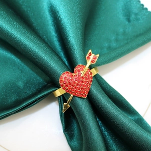 Close-up of a golden heart-shaped napkin ring with red rhinestones on green satin fabric