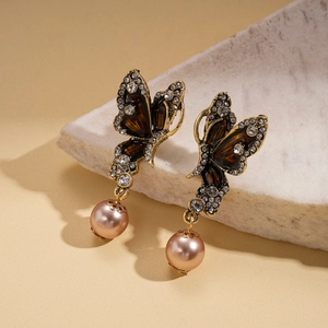 Detalle de pendientes de mariposa en bronce con cristales y colgante de perlas