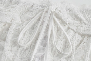 Close-up of white floral lace fabric with delicate drawstring detail on a slim fit dress
