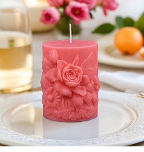 Detail van roze cilindrische kaars met reliëf van gesneden rozen en madeliefjes