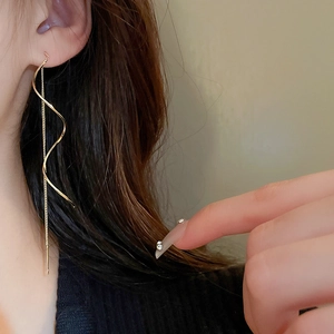 Detailed view of long gold twisted wavy threader earrings worn for a minimalist look