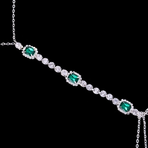 Macro detail of silver body chain featuring emerald green crystals and rhinestone fringe