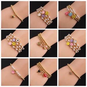 Detail of gold-plated bracelets featuring colorful enamel charms and faux pearls