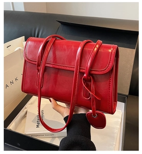 Detail of red glossy shoulder bag with heart charm against luxury gift packaging