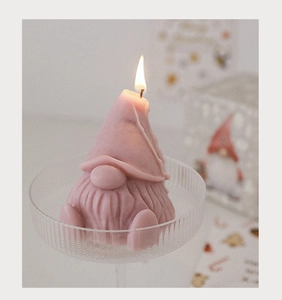 Close-up of pink gnome scented candle with burning wick on glass tray for Christmas decor