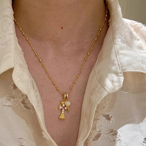 Detail von Kreuz- und Opal-Herzanhängern an goldener Perlenkette mit Spitzenoberteil