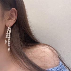 Detail of long baroque pearl tassel earrings with irregular gold lava texture studs