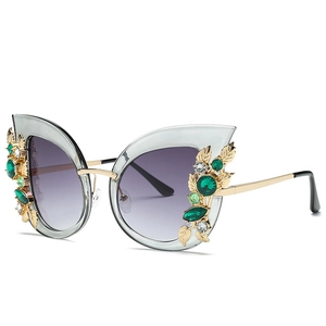 Cat eye sunglasses with gold frames, emerald stone accents, and grey gradient lenses