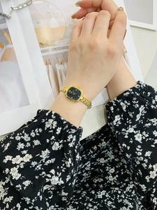 Elegant gold square watch with black dial worn on wrist against a magazine background