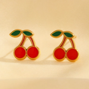 Close-up of red cherry earrings with green leaves on warm beige fabric background