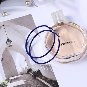 Détails de grandes créoles bleu roi mates posées près d'un flacon de parfum élégant
