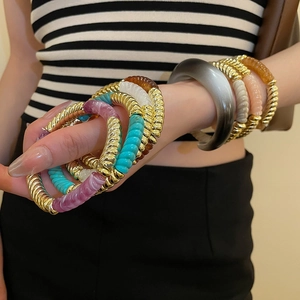 Close-up of stacked acrylic resin bracelets and golden twisted bangles on a model's wrist