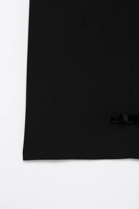 Détail de l'ourlet de robe noire avec nœud en velours et texture verticale fine
