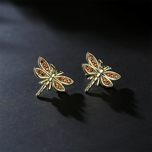Golden dragonfly stud earrings featuring amber zircon wings on dark textured background