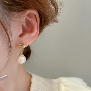 Close-up of elegant gold and pearl drop earrings worn on a model's earlobe