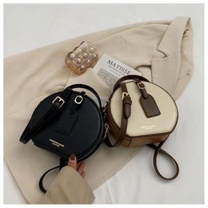 Detail of round crossbody bags in black and beige leather with gold metal hardware