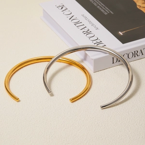 Minimalist 18k gold and silver stainless steel C-shaped open bangles on textured background