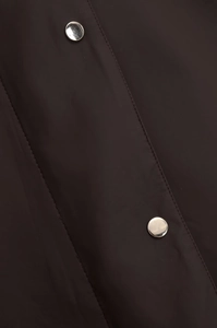Detailaufnahme der dunklen Stofftextur und der silbernen Metalldruckknöpfe an der Jacke
