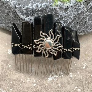 Macro detail of obsidian crystal hair comb with silver sun charm on stone surface