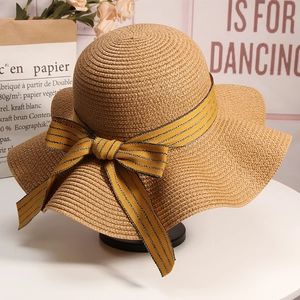 Detail of a wide brim straw sun hat featuring a yellow black striped silk bow tie