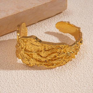 Detailed macro view of gold-toned cuff bangle with irregular lava texture and metallic finish