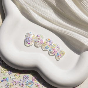 Detail of clear press-on nails featuring 3D colorful floral relief and glitter accents
