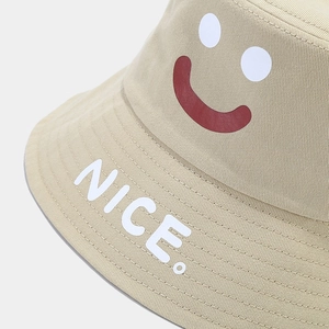 Beige cotton bucket hat featuring minimalist smiley face pattern and white NICE. text
