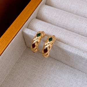 Close-up of gold C-shaped earrings with diamond-grid texture and colorful gems