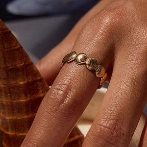 Macro detail of gold stainless steel seashell ring on hand with summer cone backdrop
